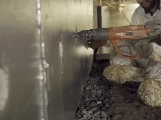 Technician using a power tool to fasten a sheet liner to a crawl space foundation wall above gravel