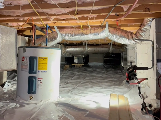 Clean crawl space with white plastic ground liner, a water heater and insulated ducts under the floor joists