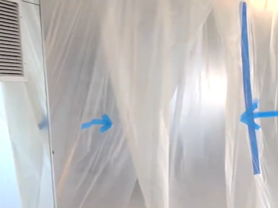 Clear plastic sheeting taped with blue tape forming a containment barrier next to a wall vent
