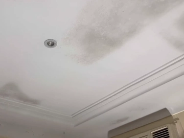 Ceiling with dark patches near a vent, with an air conditioning unit in the corner