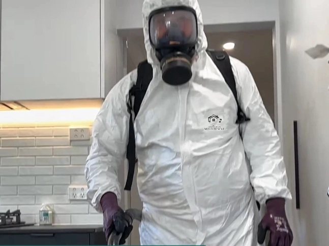 Technician in a white protective suit and respirator with a backpack HEPA vacuum in a kitchen
