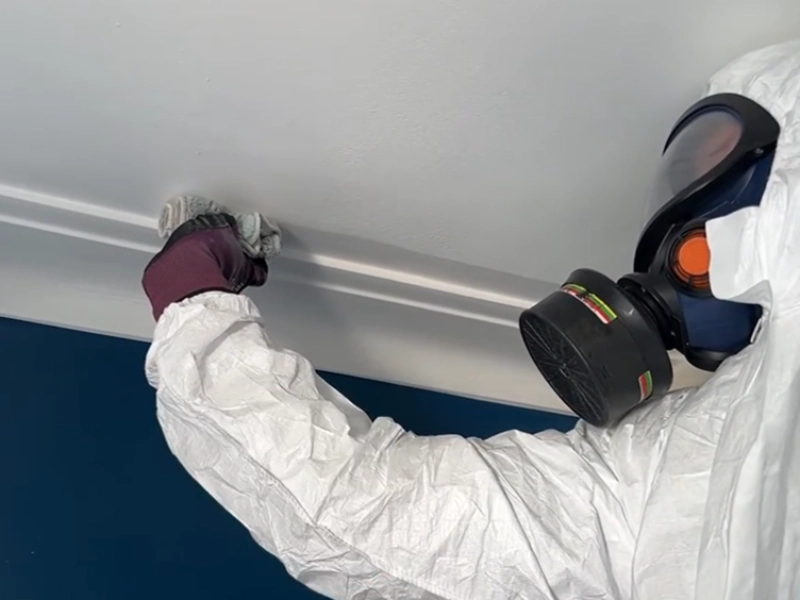 Mold removal technician in a protective suit and respirator working at a ceiling joint in a High Springs home